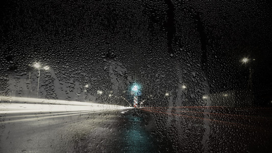 通过玻璃与雨滴的道路的夜景图片