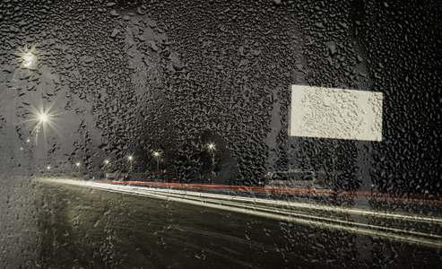 通过玻璃与雨滴的道路的夜景图片