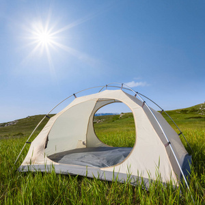 在闪耀的阳光下的绿山间白色旅游帐篷
