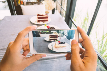 手拿着智能手机和拍照的美味蛋糕的