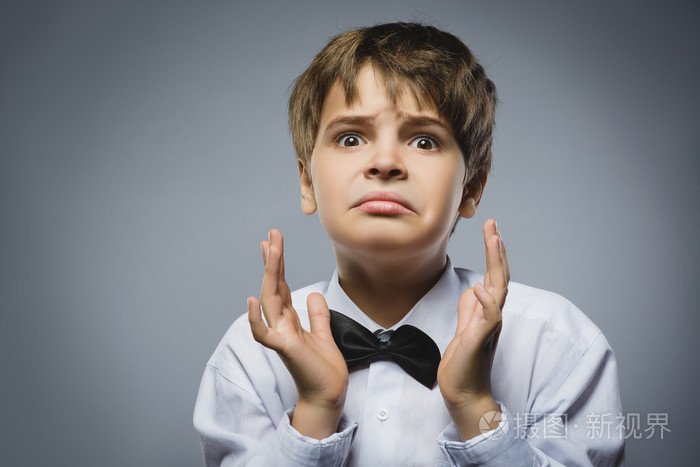 英俊的男孩,而站在灰色背景下的惊讶表情的特写肖像