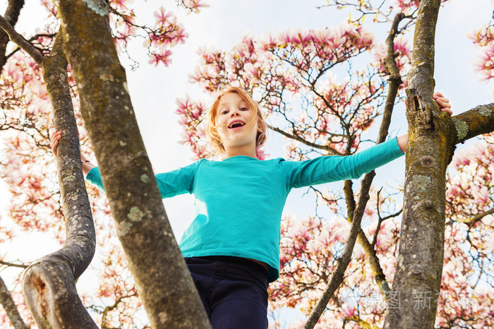 可爱的小红发女孩在漂亮的木兰树上玩耍