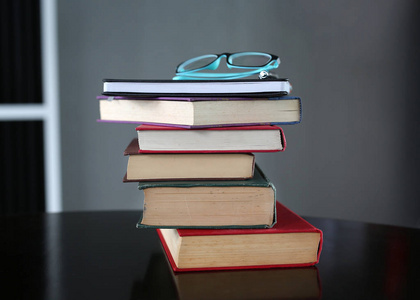 堆栈的精装书，戴着眼镜木制的桌子上。教育背景