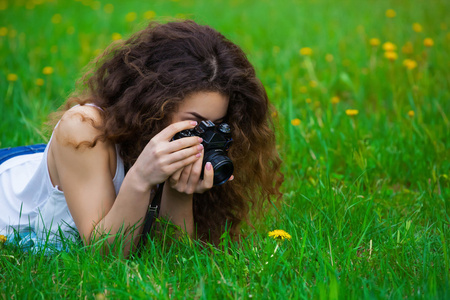 美丽的女孩摄影师与卷曲的头发，我躺在草地上