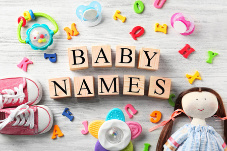 多维数据集与文本的婴儿名字 玩具 安抚奶嘴 塑料字母和鞋子在木制的背景上