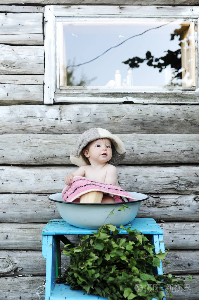 小漂亮的女婴,在碗里洗碗的背景墙的木房子