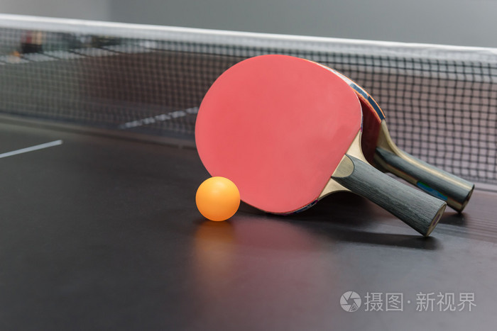 橙色的球,用黑色的桌子上的红色乒乓球球拍