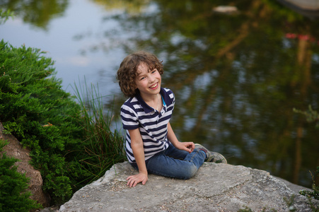 微笑的男孩坐在池塘边