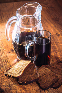 俄罗斯酿造酒在杯壶和面包的黑麦面粉对木制背景