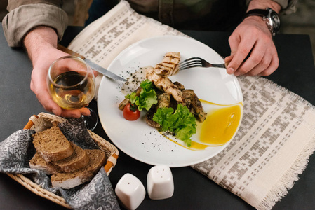男士特写在餐桌上用叉子和小刀在白色盘子上吃可口的烤肉和蔬菜