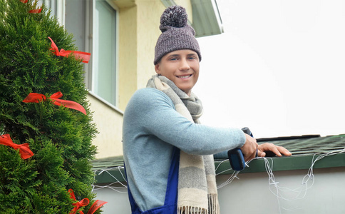 年轻男子挂圣诞灯在房子的屋顶上
