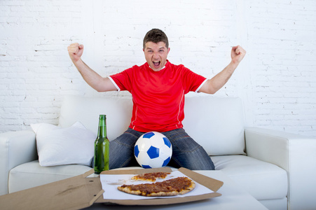 电视上观看比赛的球队球衣庆祝目标疯狂快乐在沙发上的年轻的足球风扇人