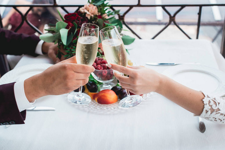 在新娘和新郎的手杯香槟饮料。快乐的新婚夫妇喝酒。爱的情侣创造了新的家庭