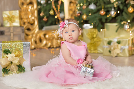 圣诞节快乐滑稽的婴孩享受工作室装饰在休闲椅子沙发上的粉红色礼服新年临近圣诞节树