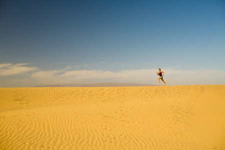 年轻女子在沙漠沙丘上运行