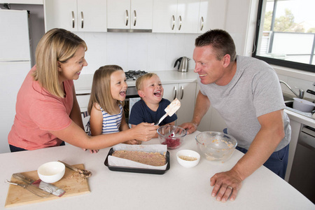 年轻幸福夫妇一起烘烤与小儿子和年轻漂亮的女儿在家厨房玩奶油的乐趣