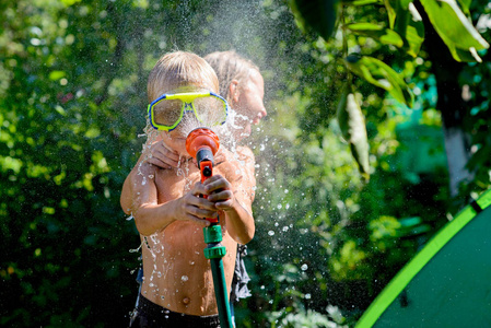 快乐的男孩玩水。那男孩手里拿着一根花园水管。关注男孩