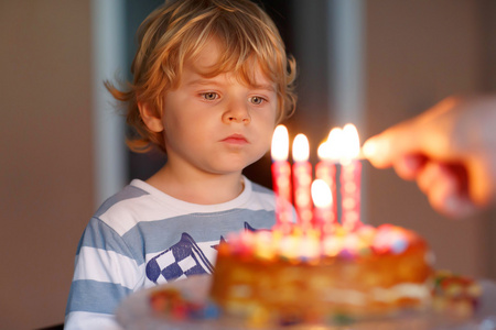 被裁剪男孩在家庭聚会上吹灭生日蛋糕蜡烛小小孩男孩庆祝他的生日和