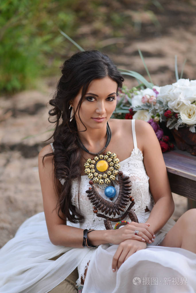 穿着白衣的女人坐在沙滩上波西米亚风格的新娘