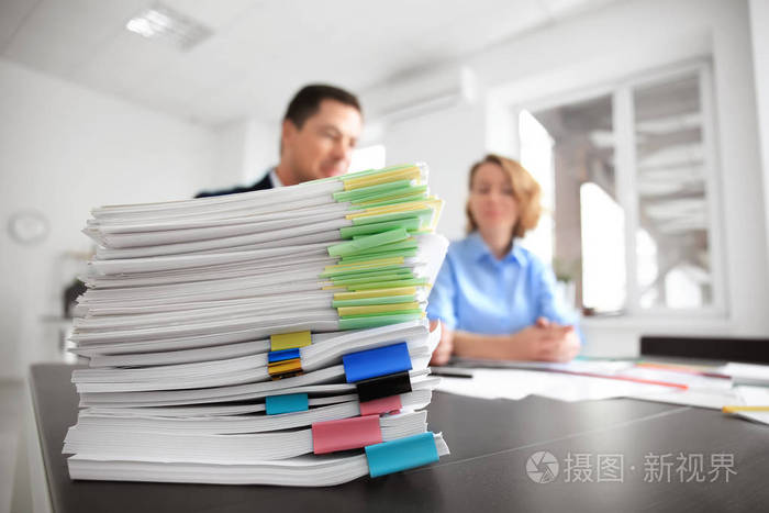 桌子上的成堆的文件和办公室里模糊的工人