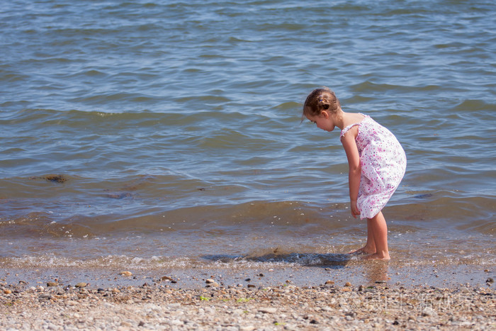 小女孩穿着长裙寻找贝壳和石头在大海的岸边