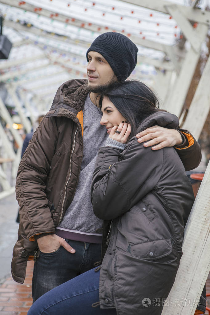 夫妇穿着休闲灰色的衣服和拥抱对方.寒冷的天气, 背景下的圣诞灯