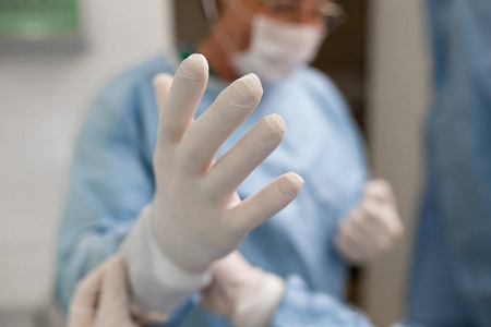 外科医生正在准备手术。助手帮助经验丰富的首席外科医生戴上无菌橡胶手套。医学外科急救概念
