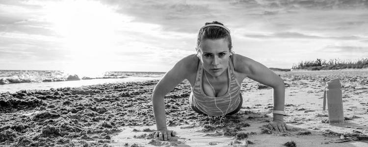 清新的野海边锻炼。年轻的运动员在沙滩上做俯卧撑的运动服装