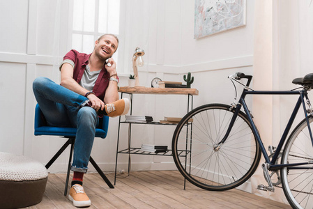 微笑的人谈论智能手机, 而坐在家里的椅子上自行车