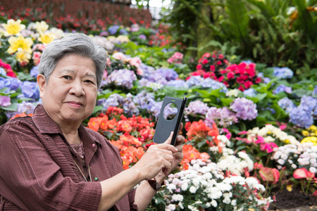 在花园里手持手机的老妇人。老年女性展览会