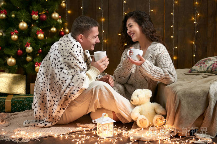 快乐的情侣喝茶, 在圣诞装饰, 坐在地板上, 在黑暗的木制室内灯.