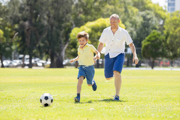 年轻快乐的父亲和兴奋的小7或8岁的儿子一起玩足球在城市公园花园运行