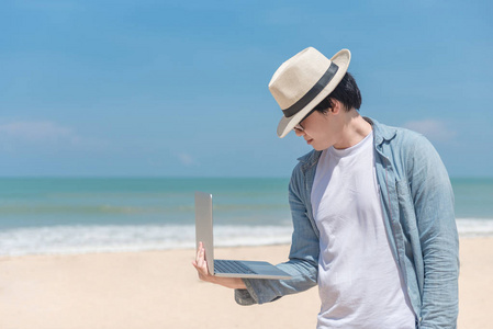 亚洲年轻男子拿着笔记本电脑在海滩上