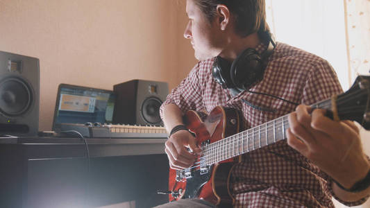 年轻音乐家作曲和录制原声吉他使用电脑, 耳机和键盘