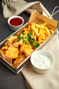 炸鸡块配薯条和木板上的不同调味汁照片