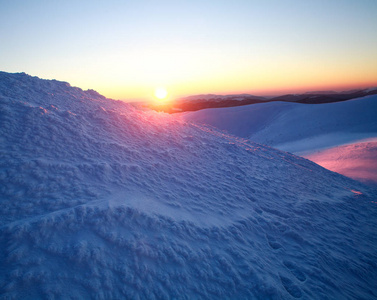 天空背景下白雪皑皑的冬山之上的日落