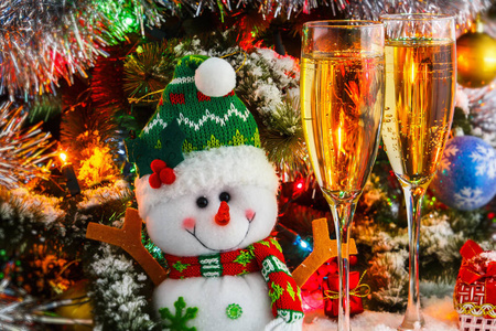 圣诞雪人和与背景下的一棵圣诞树的起泡酒的酒杯。球，花环，金属丝