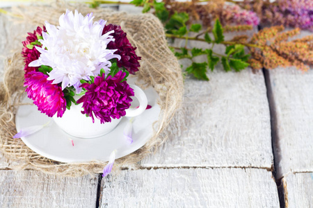 在白色的木制背景上有花紫花瓣的杯子。最小的概念。平躺
