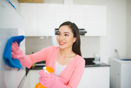 有吸引力的年轻妇女的画像用洗涤剂喷雾清洗白色厨房衣柜的表面