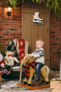 俏皮的微笑的快乐可爱的小男孩穿着毛衣和牛仔裤坐在摇椅在装修的新年房间在家里。圣诞节好心情。生活方式, 家庭和假日2018概念