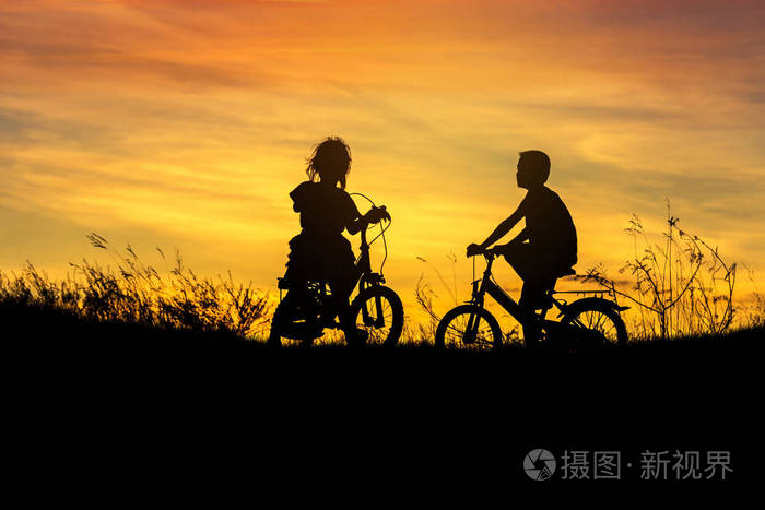 在日落剪影小男孩和小女孩骑自行车