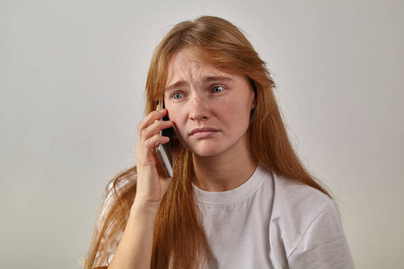 年轻的红头女人与雀斑的肖像手持电话旁边的耳朵和说话悲伤的表情在脸上