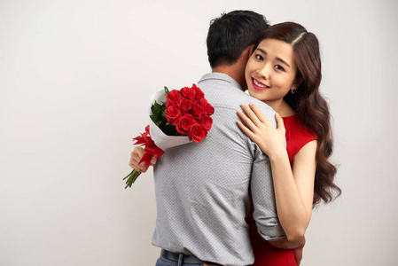 迷人的亚洲女人在拥抱她的男友时, 带着妩媚的微笑看着镜头, 与世隔绝的白色背景