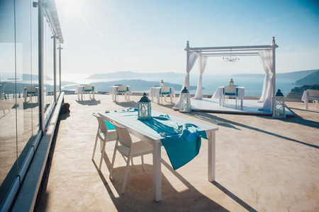 白色拱门为婚礼在露天与灯笼和平台与白色家具在海, 海岛和蓝天在圣托里尼岛的背景