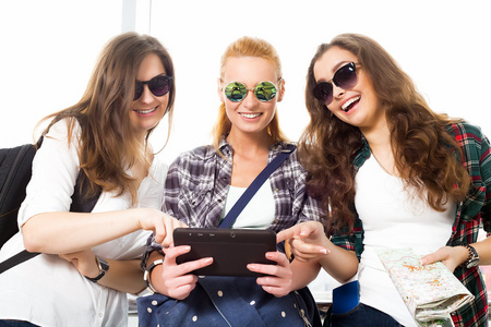 三个女孩站在机场，看着这款平板电脑。和朋友一起旅行