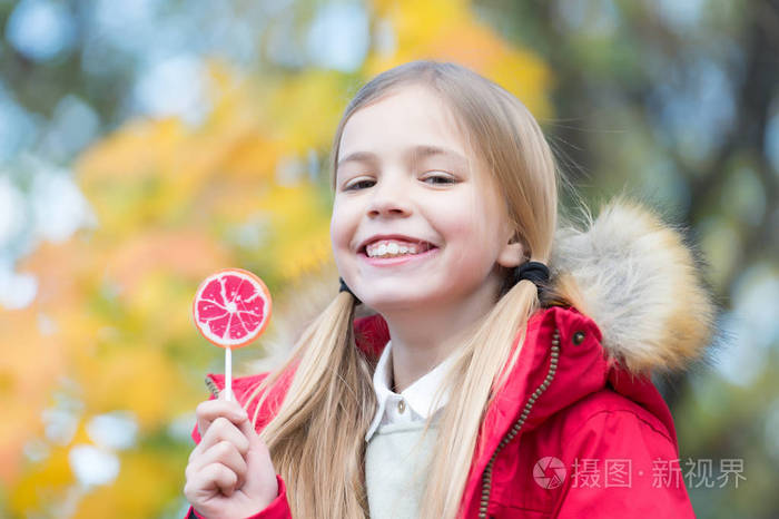 女孩的微笑与棒糖在自然背景.孩子微笑与糖果在棍子室外.