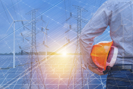 安全电压双曝光工程师站举行黄色安全帽与风力涡轮机和高电压电力支柱