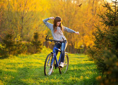 快乐的女孩与手臂伸出自行车和看的看法, 在一个绿色的草地在日落