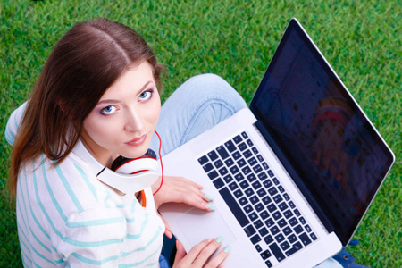 坐在绿草地上的手提电脑的年轻女子。Portreit 年轻妇女