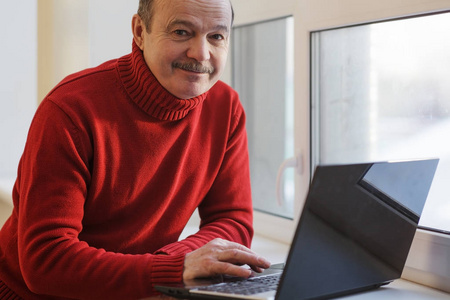 穿着红色毛衣靠窗笔记本电脑上工作的人。在成年后做自由职业者